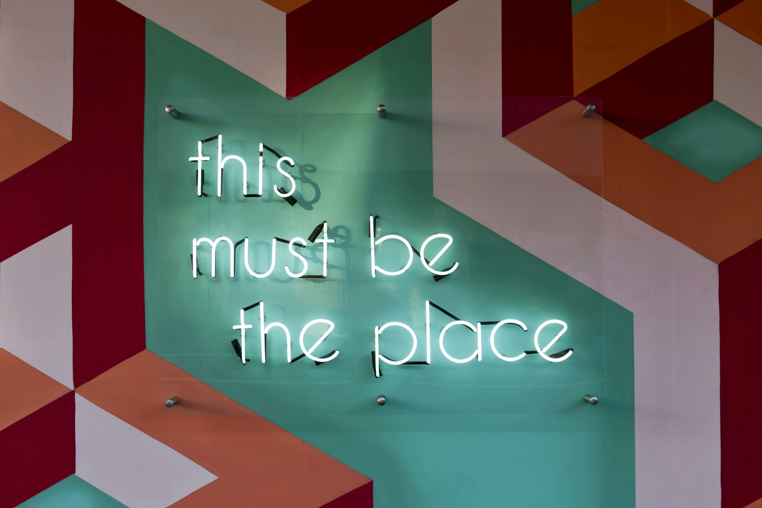 Colorful geometric mural with a neon sign that says 'this must be the place'