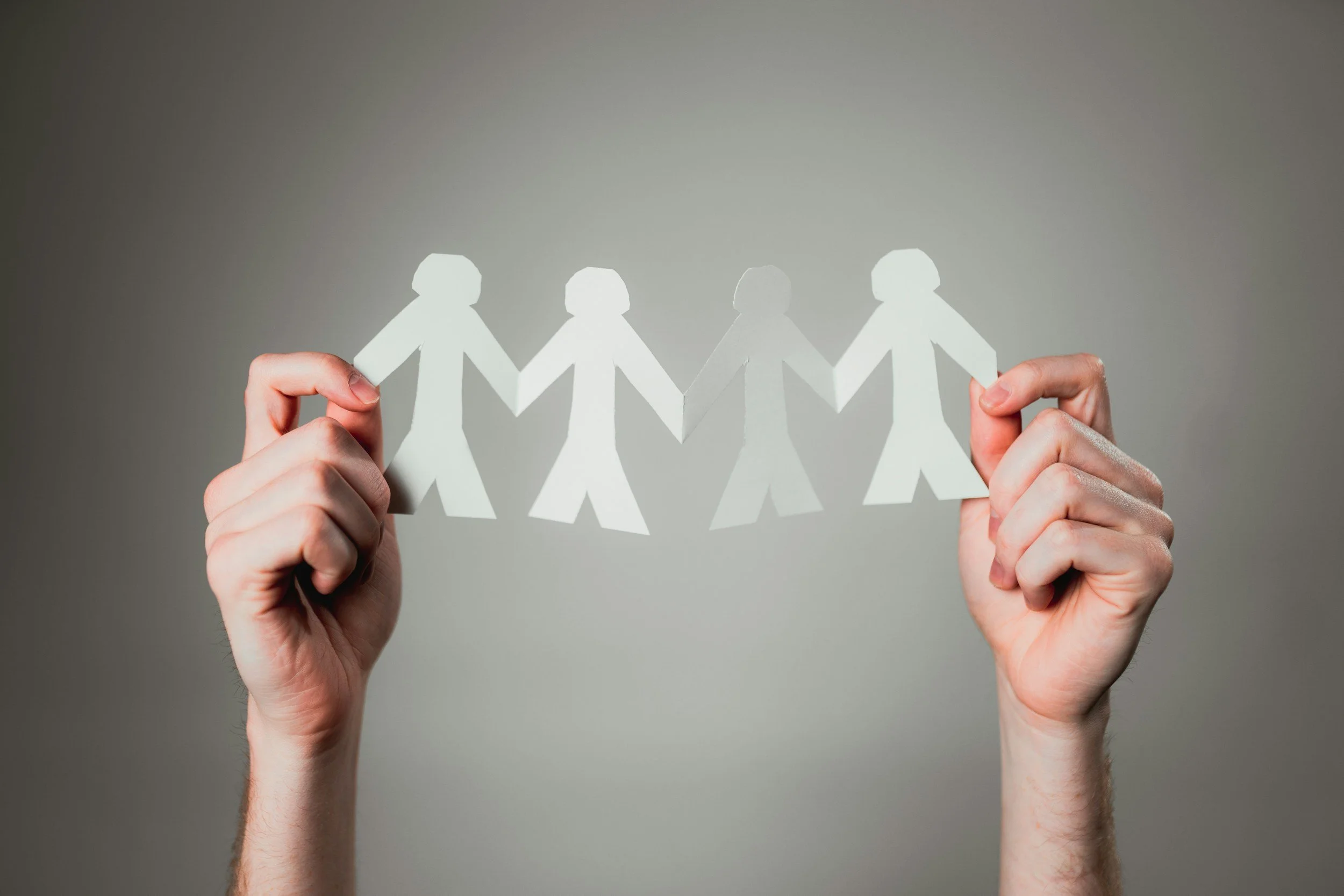 Hands holding a paper chain of people figures, symbolizing connection or unity.