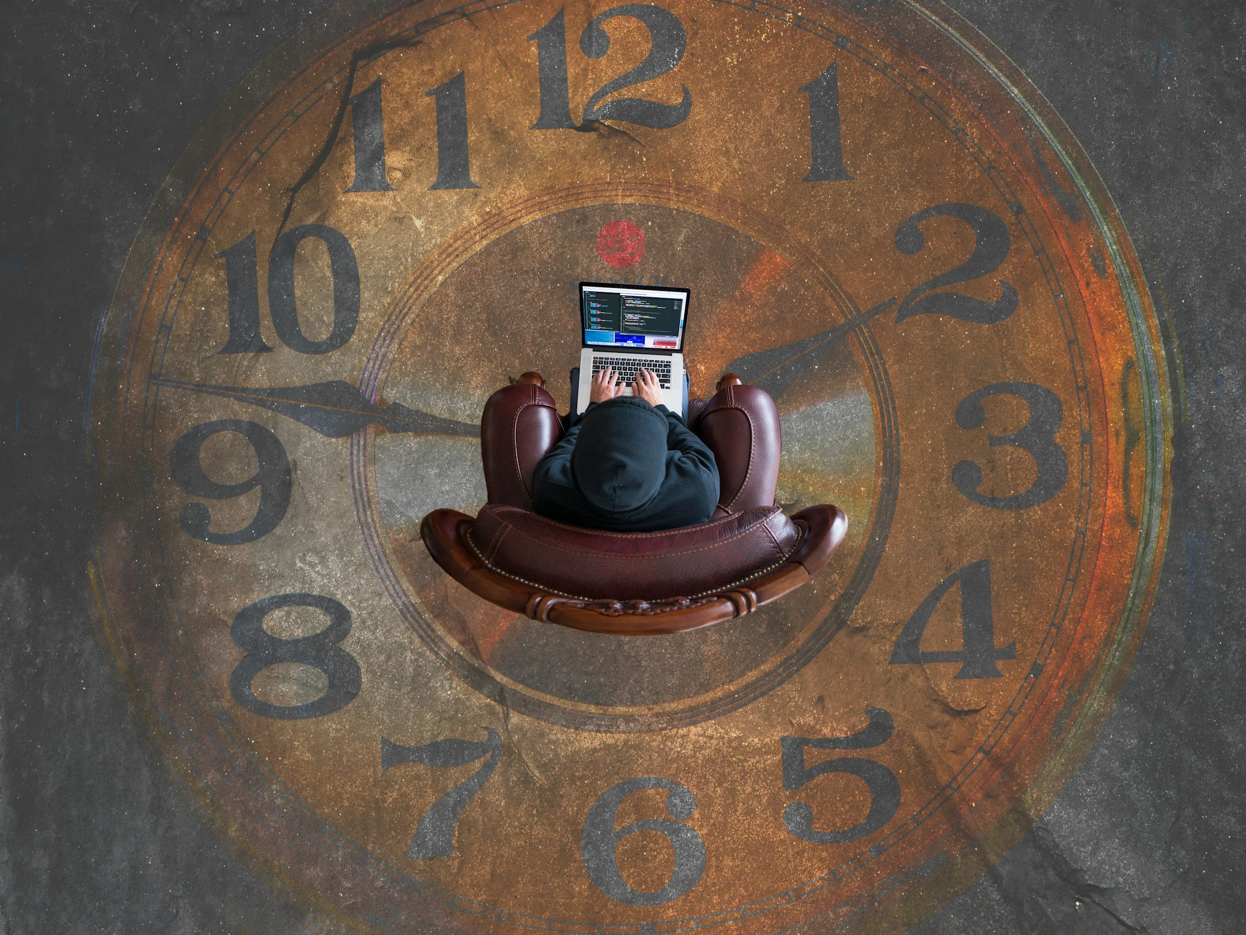 Person sitting in a leather chair using a laptop, with a large, vintage clock face in the background.