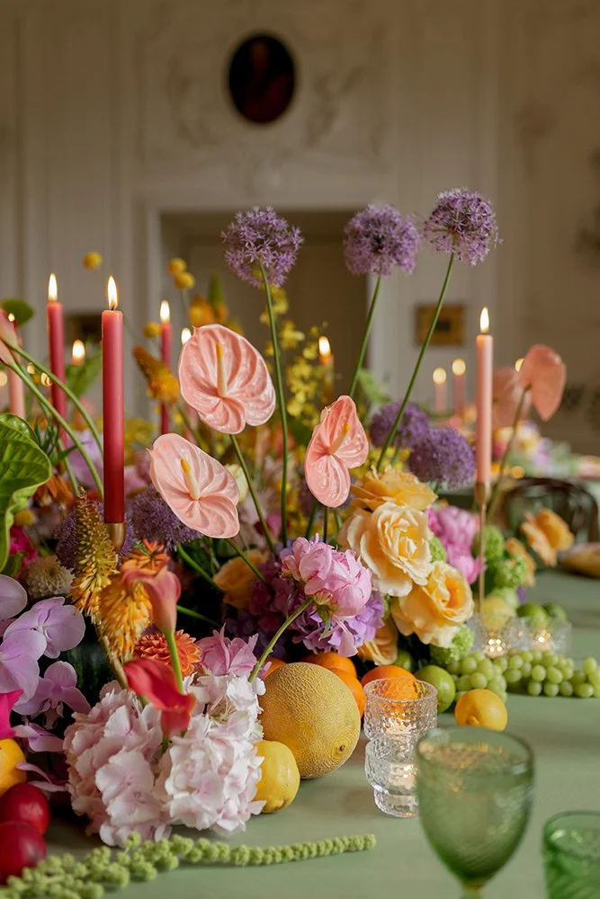 Bunte Blumen und Stabkerzen sind auf einem grünen Tisch platziert.