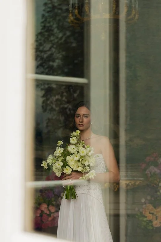 Eine Frau steht hinter einem Fenster und hält einen Blumenstrauss.