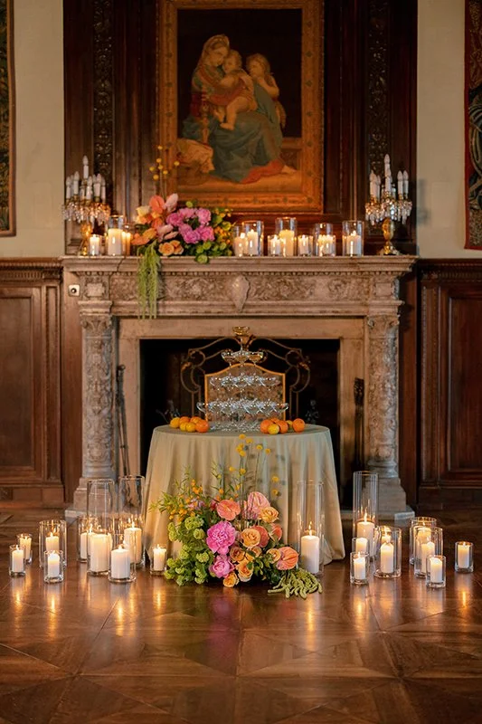 Ein grüner Tisch mit Gläsern steht vor einem Chemine mit Blumen und Kerzen.