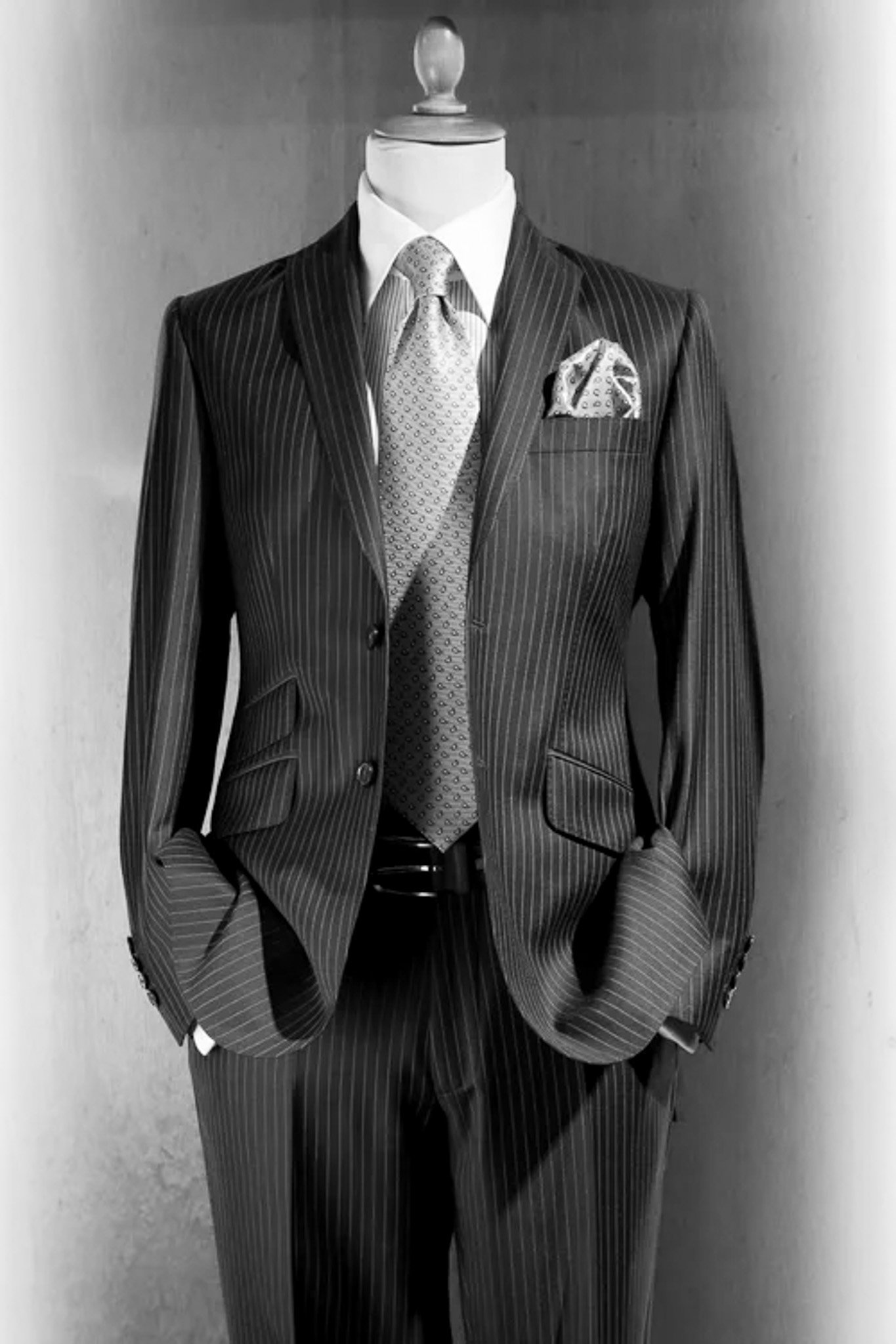 Schwarzer Anzug mit feinen weißen Streifen, weißes Hemd, gemusterte Krawatte und Einstecktuch, an einem schwarzen Krawattenhalter, auf einem Puppenmodell