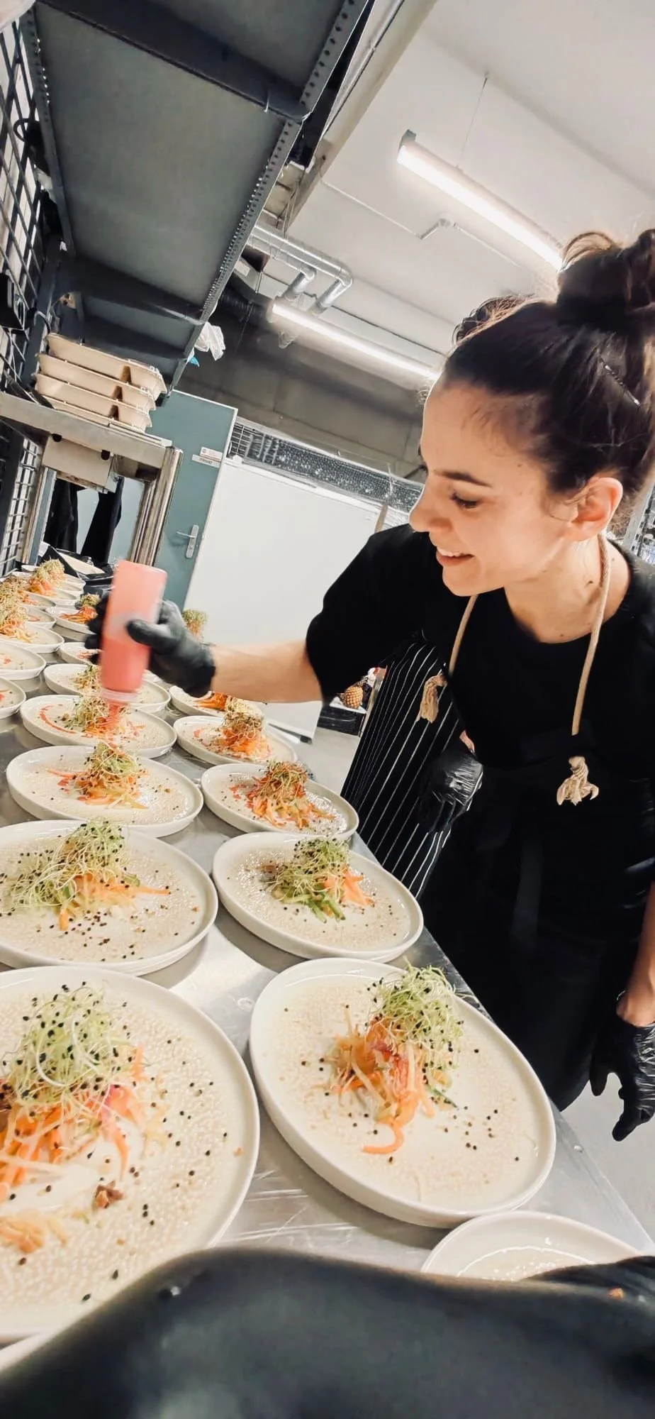 Küchenmitarbeiterin dekoriert Teller mit Spargel und Karotten, in einem Küchenraum mit Lichtrauch.