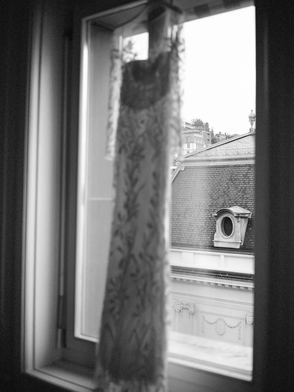 Ein schwarz weiss Bild von einem Brautkleid, dass an einem Fenster hängt.