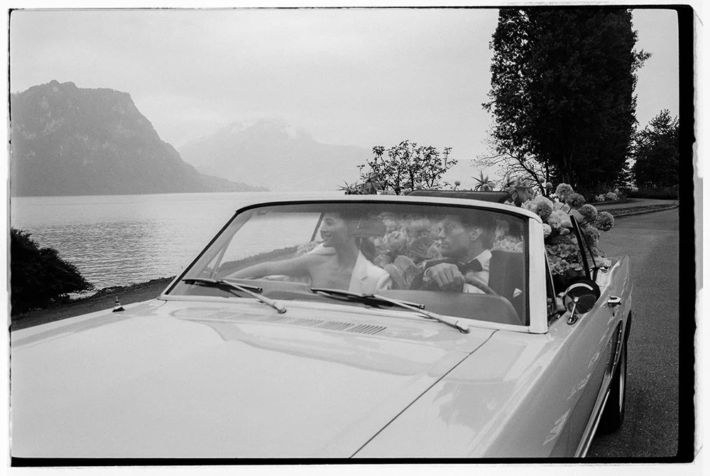 Ein schwarz weiss Bild von einem Paar in einem Oldtimer am Wasser.