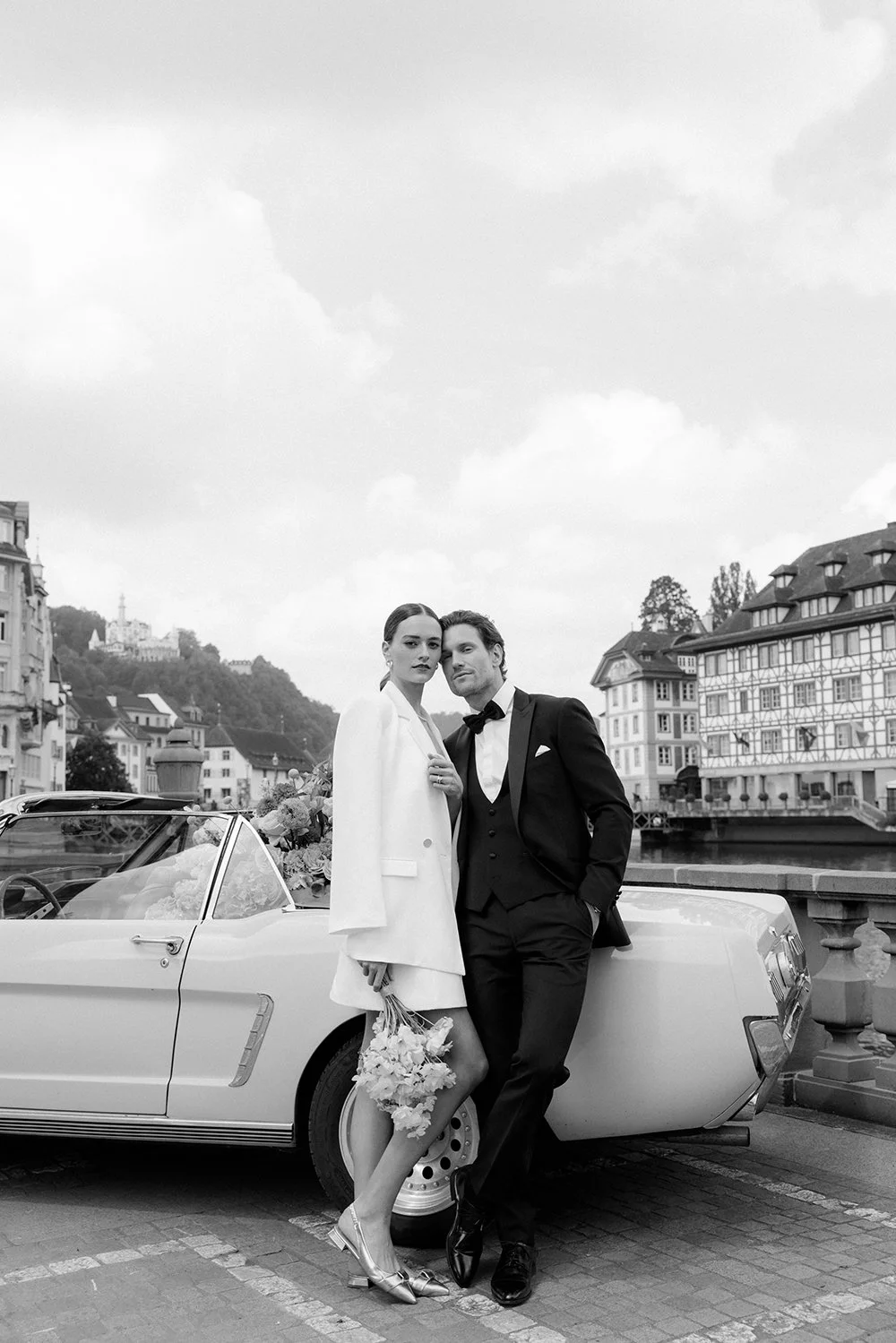 Ein schwarz weiss Bild von einem Ehepaar vor einem alten Auto.