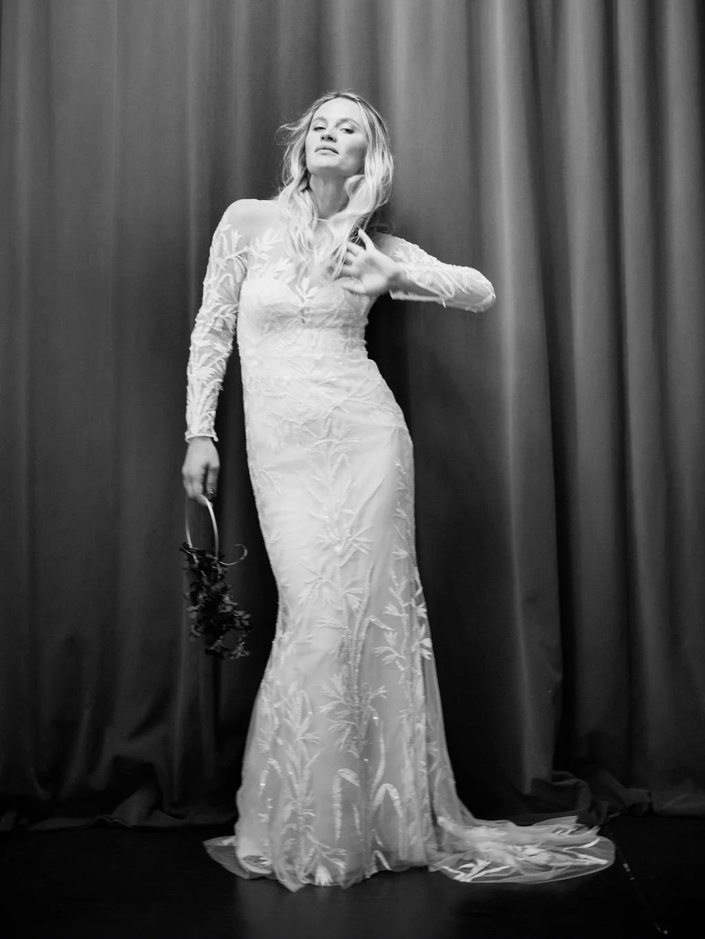 Eine Frau in einem weissen Kleid steht vor einem dunklen Vorhang.