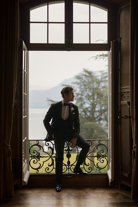 Ein Mann sitzt im Anzug auf einem Geländer in einem grossen Fenster.