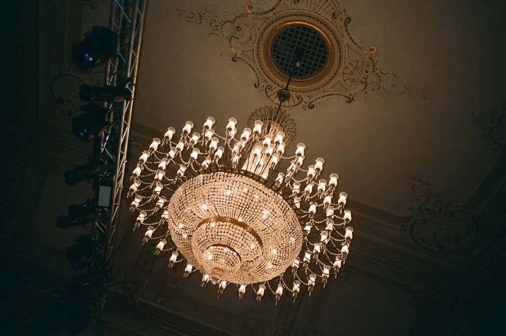 Ein grosser runder Kronleuchter hängt an einer Decke mit Stuckaturen.