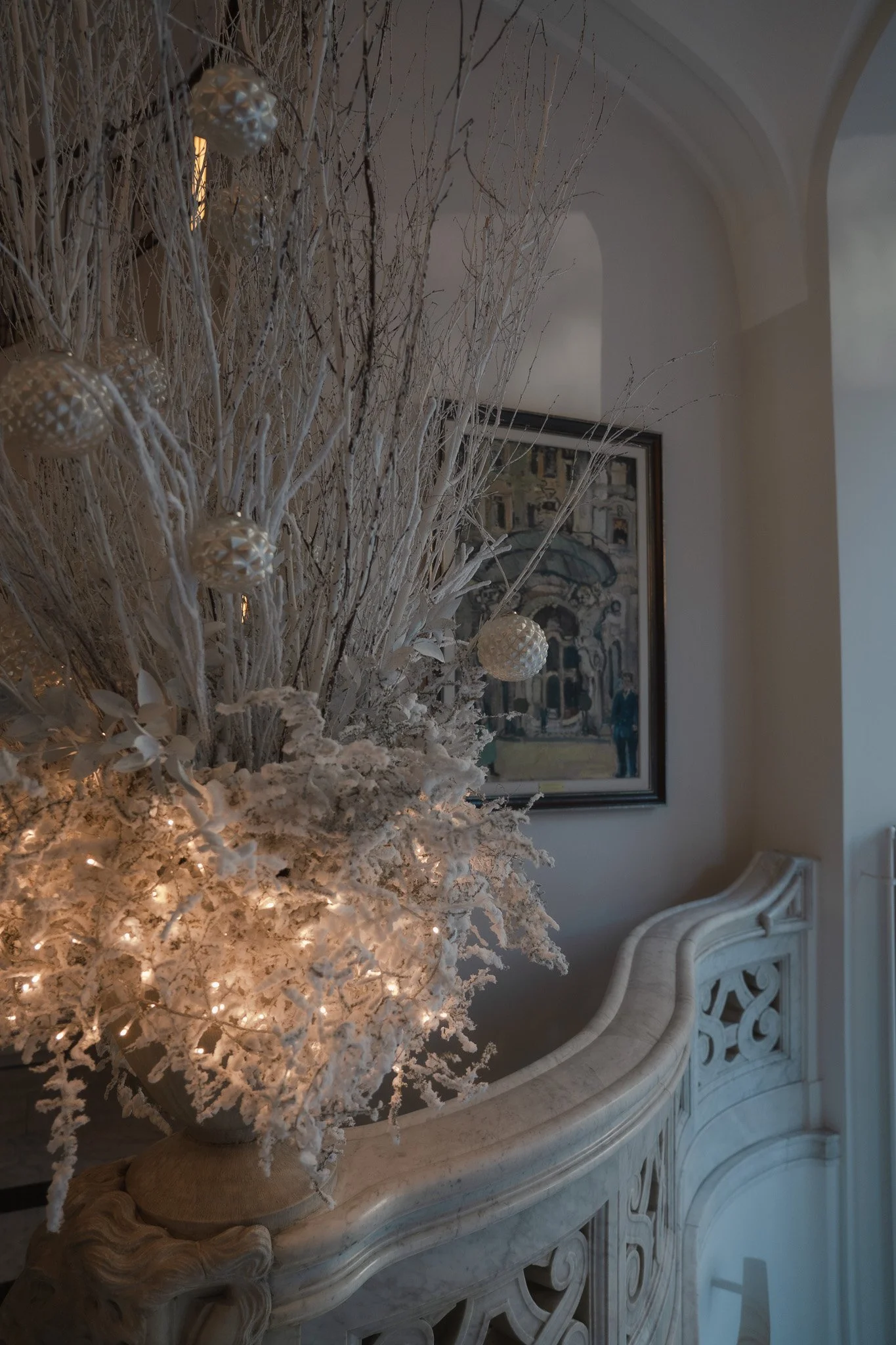 Ein weisses Blumengesteck steht auf einer Ablage und ist beleuchtet mit einer Lichterkette.