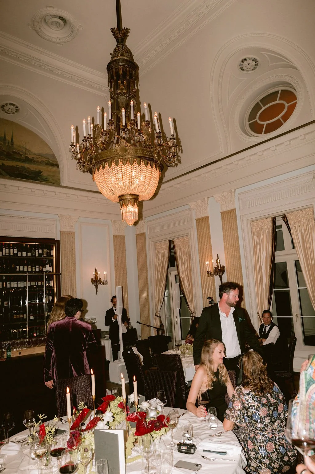 Ein Raum mit Kronleuchter und Leuten die an einem eingedeckten Tisch sitzen.
