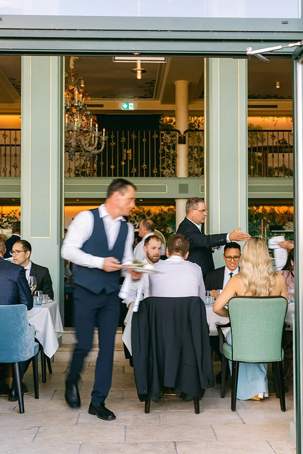 Leute sitzen an Tischen und werden von einem Kellner bedient.