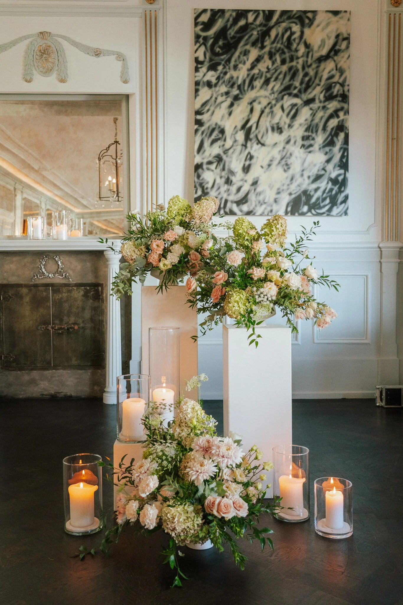 Blumenarrangements sind auf weissen Säulen platziert neben leuchtenden Kerzen in Gläsern.