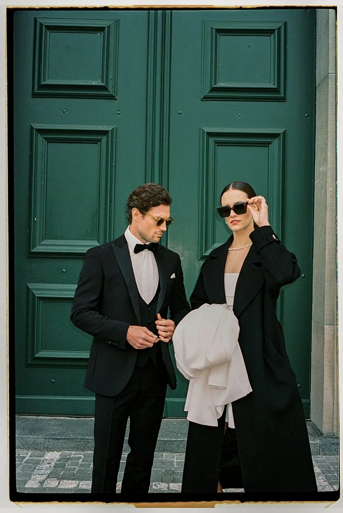 Ein Paar im Anzug und Mantel stehen vor einer grossen grünen Türe.