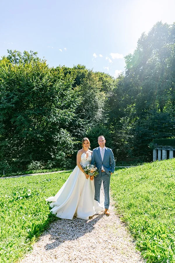 Ein Brautpaar steht in einem Garten lachend nebeneinander.