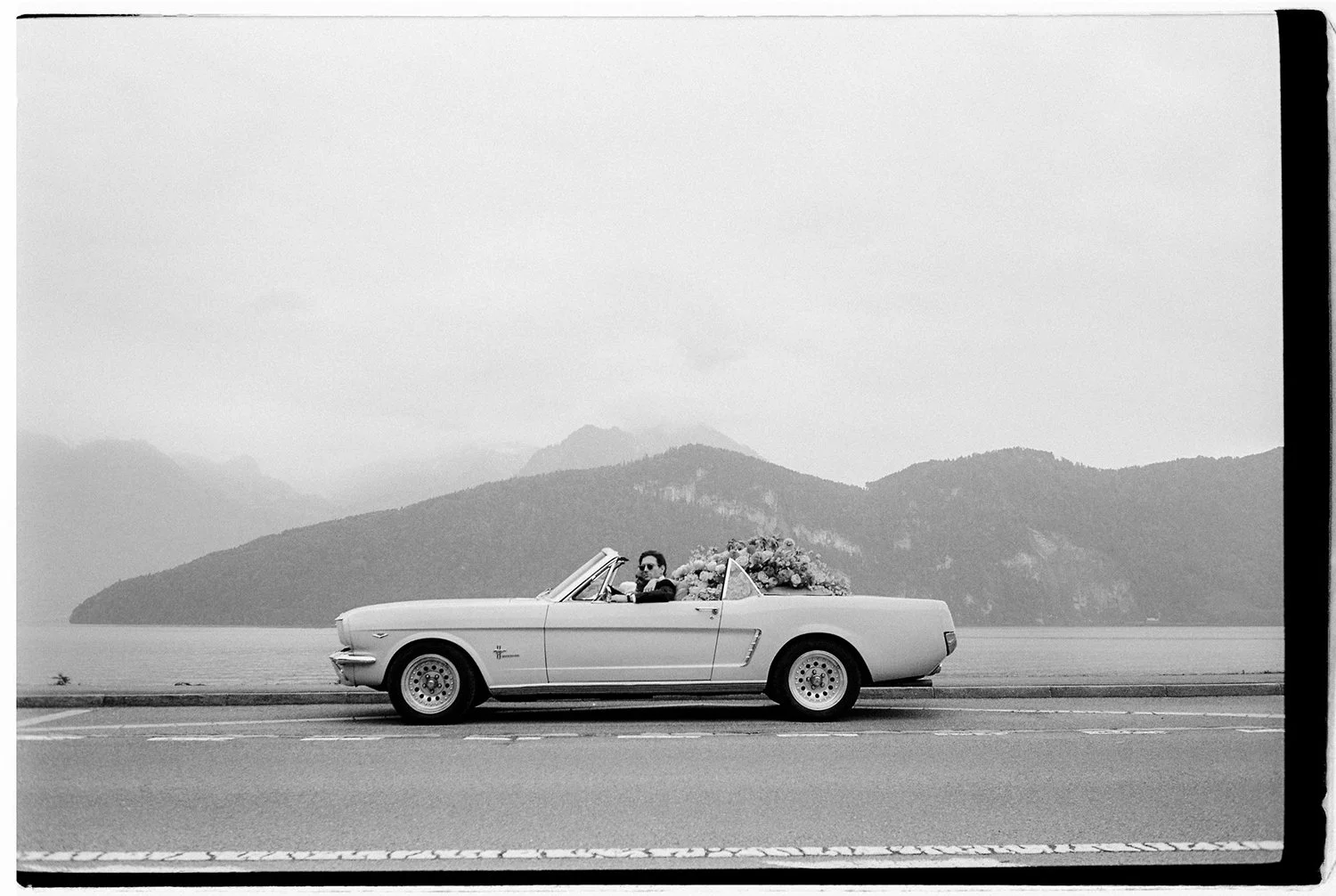 Ein Oldtimer steht gefüllt mit Blumen auf der Strasse vor einem Bergpanorama.