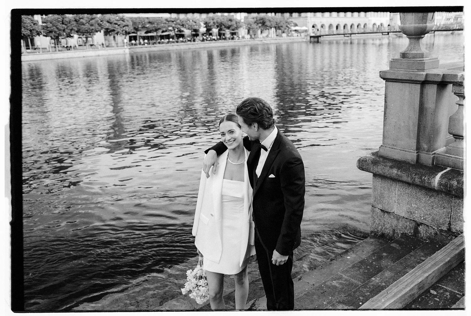 Ein schwarz weiss Foto von einem Paar, dass am Wasser steht und lächelt.