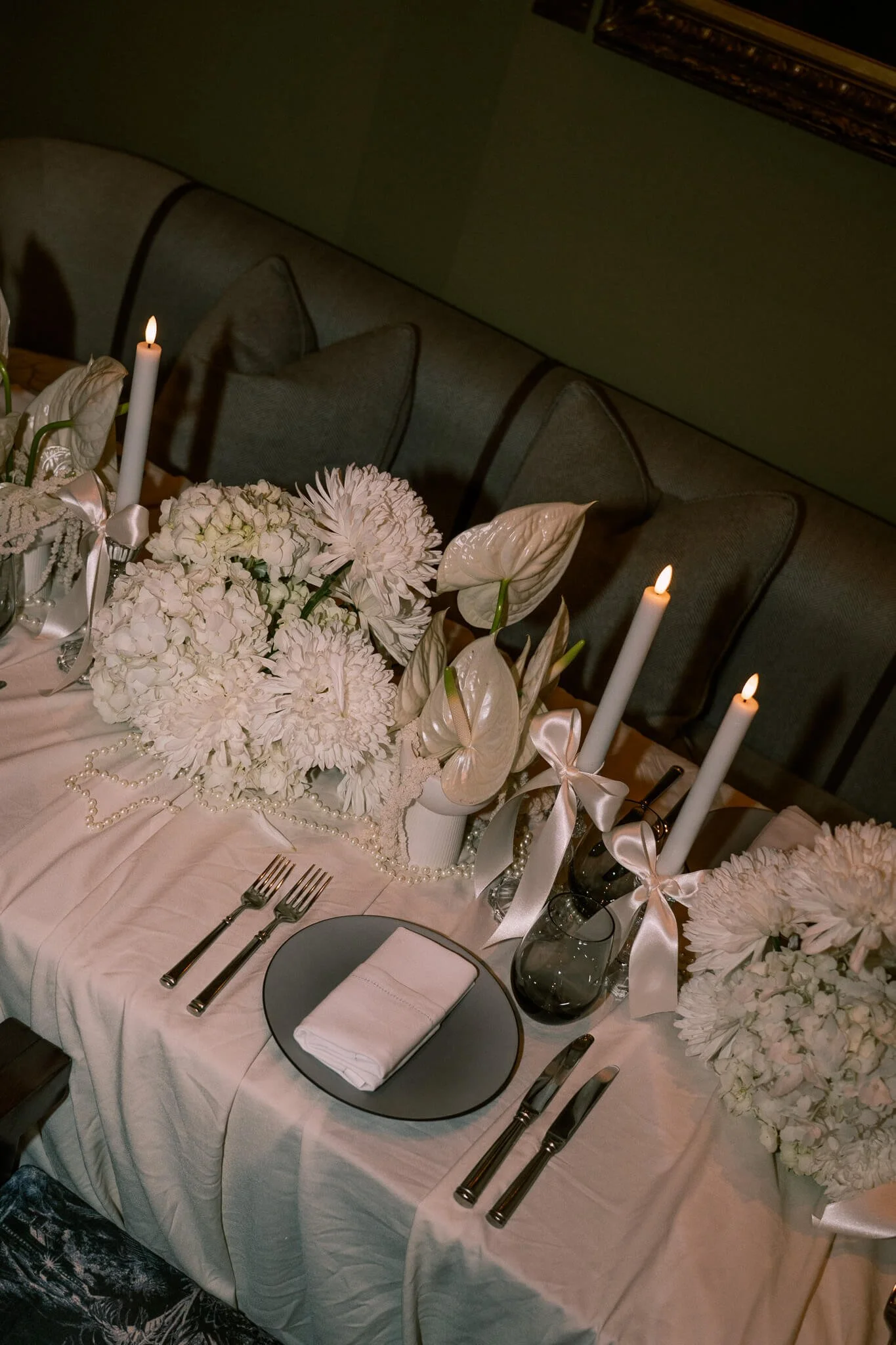 ein eingedeckter Tisch mit weissen Blumen, Stabkerzen und Perlen.