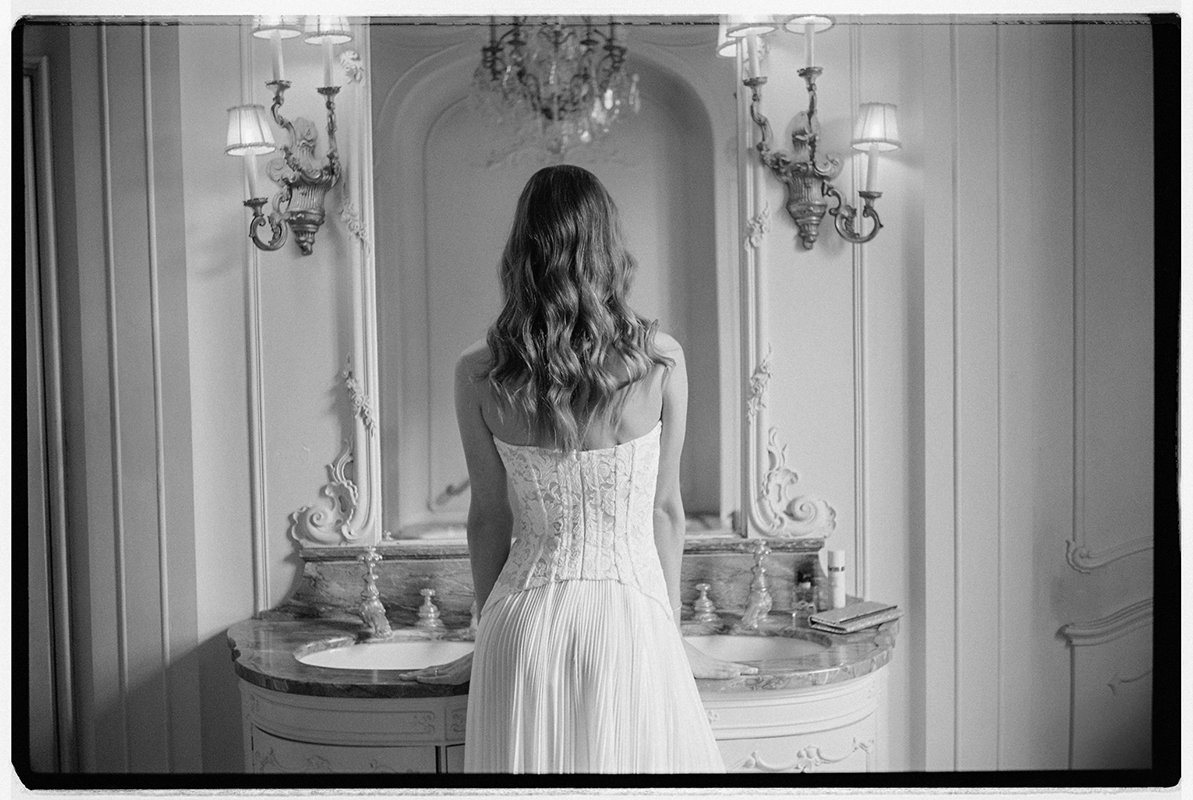 Eine Frau steht in einem weissen Kleid vor einem Spiegel.