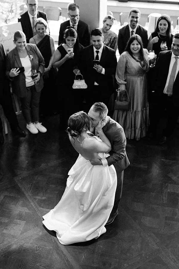 Ein schwarz weiss Bild von einem küssenden Brautpaar umgeben von Leuten.