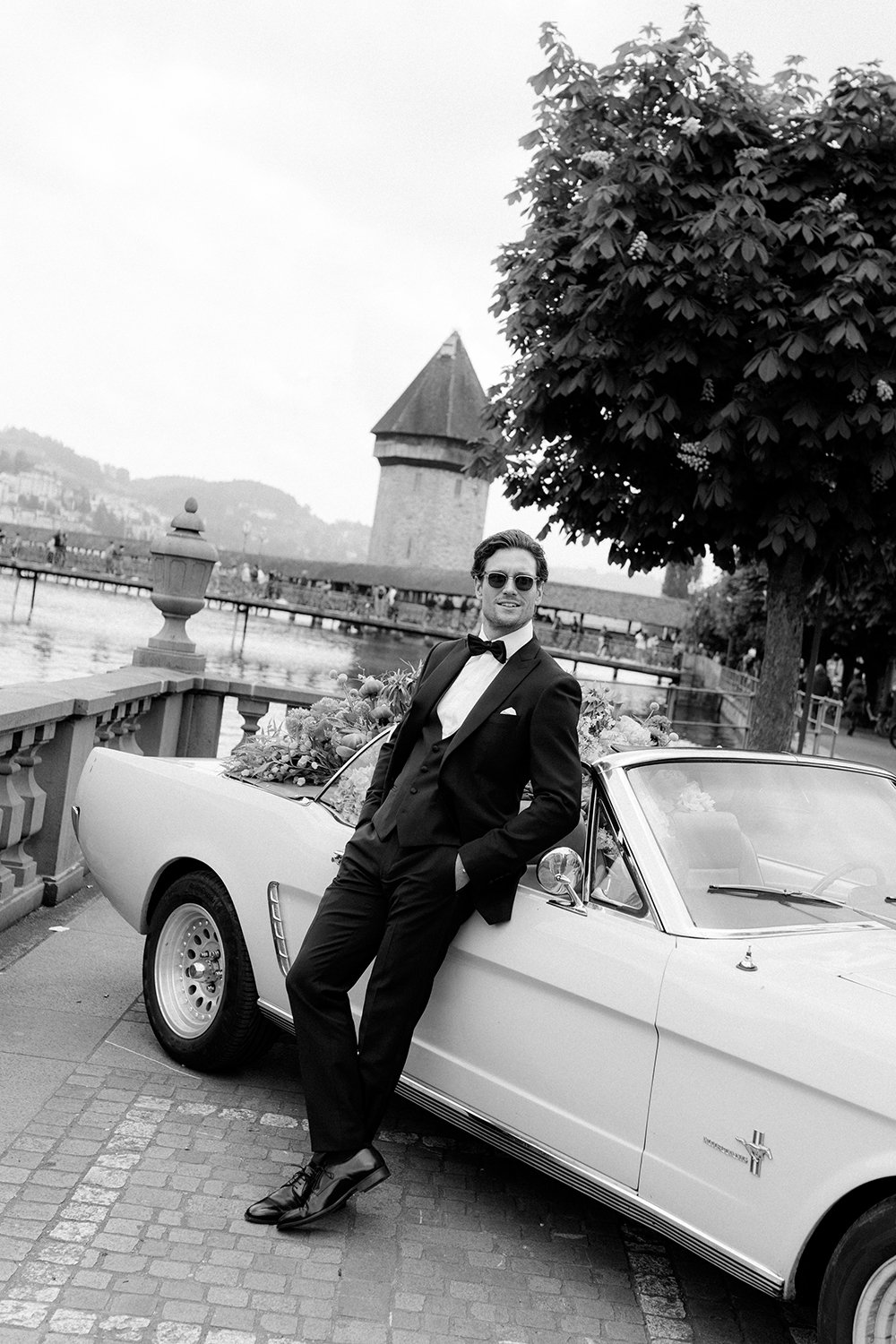 Ein Mann im Anzug steht vor einem Oldtimer bei der Kappelbrücke.