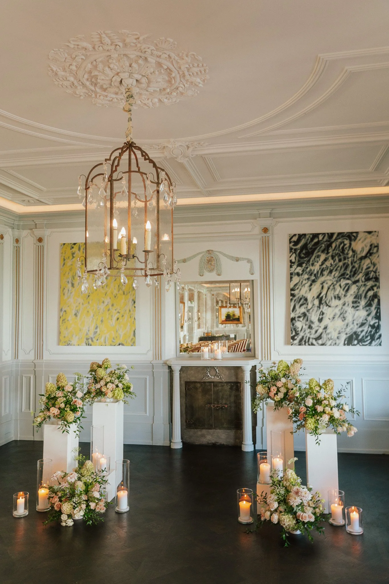 Blumengestecke sind auf weissen Säulen arrangiert mit weissen Kerzen in einem romantischen Raum.