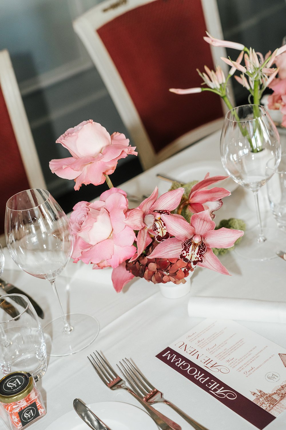 Auf einem weissen Tisch steht ein kleines Blumenarrangement aus pinken Blüten.
