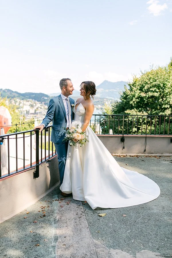 Ein Brautpaar steht auf einem Balkon im Sonnenlicht und lächelt sich an.