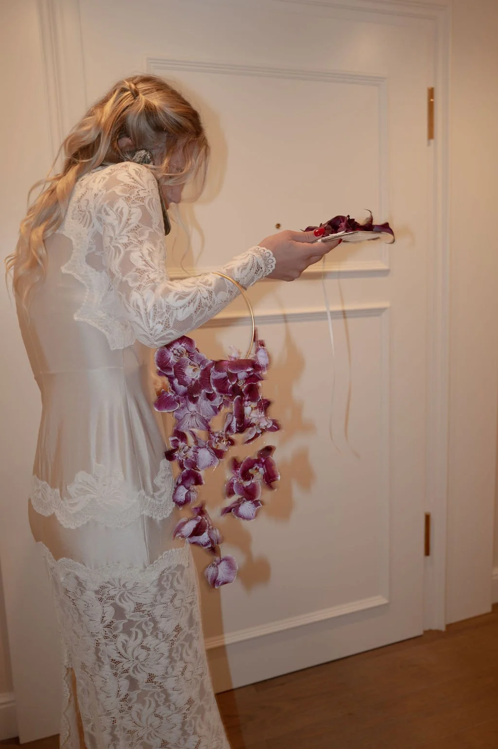 Eine Frau in einem weisen Kleid ist am Telefon und hält einen Ring mit violetten Blumen.