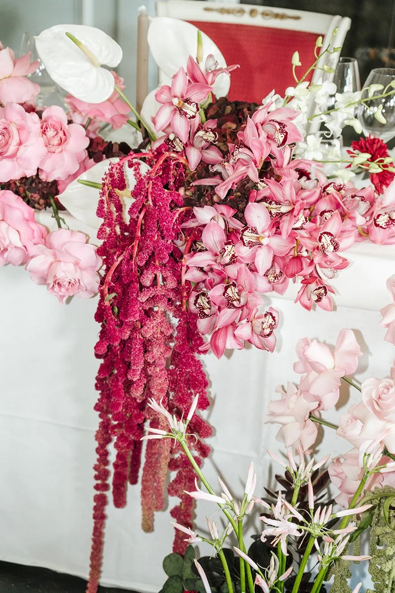 Auf einem weissen Tisch ist ein grossen Blumenarrangement mit pinken und grünen Blumen platziert.