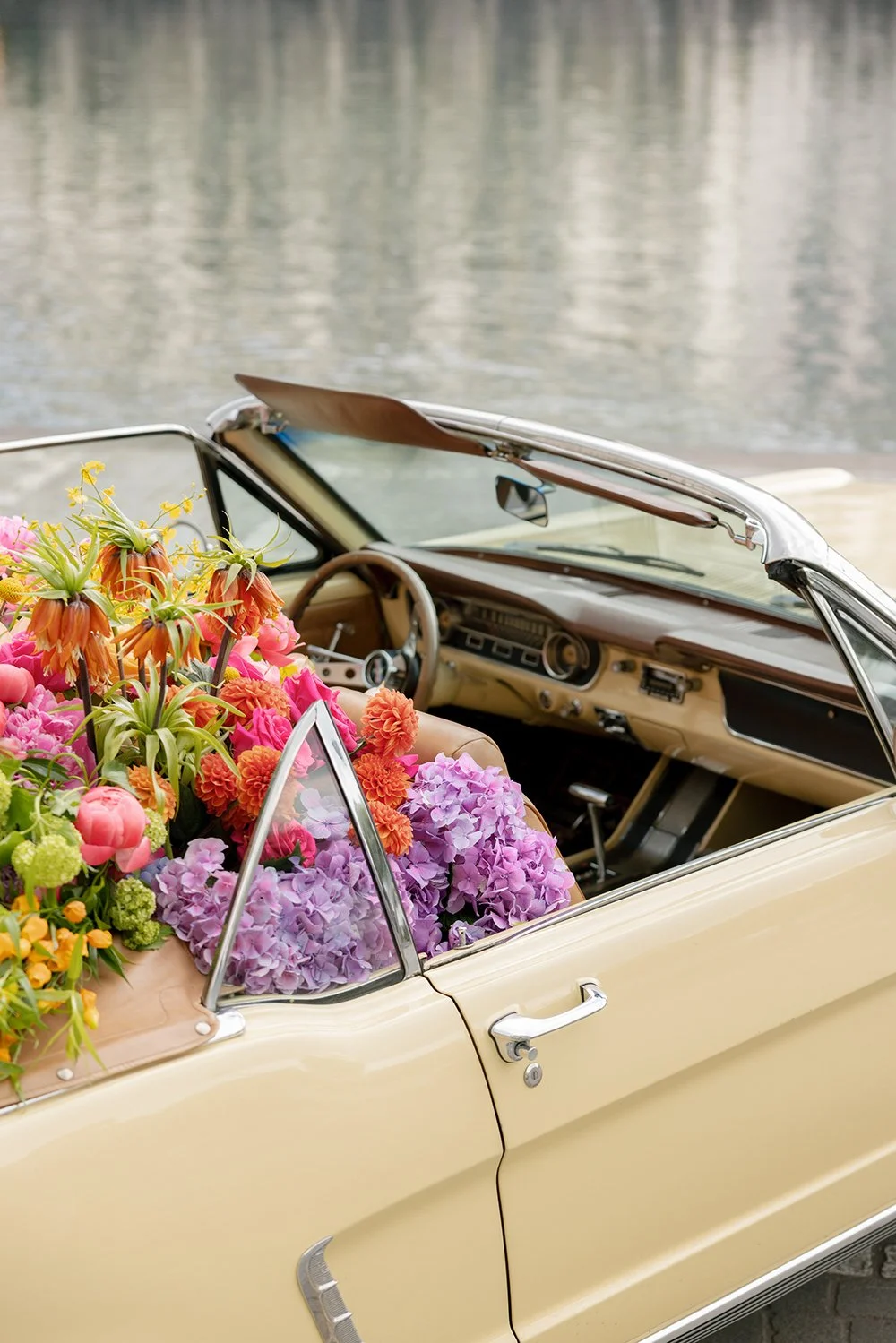 Ein hellgelber Oldtimer Cabriot steht auf der Strasse und ist gefüllt mit bunten Blumen.