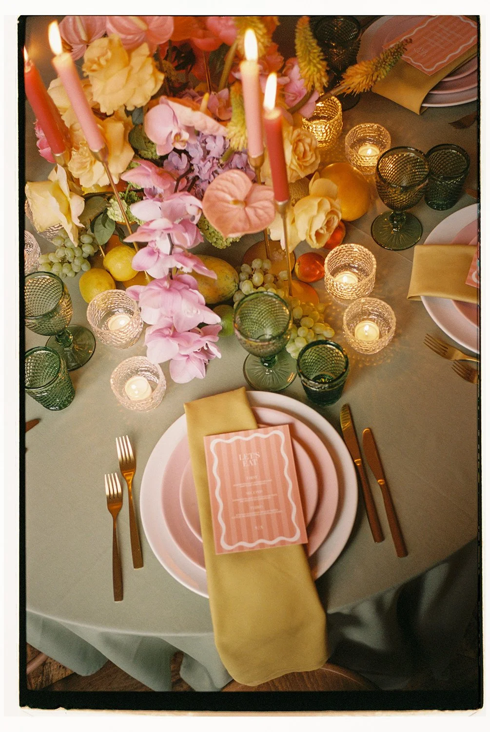 Ein eingedeckter grüner Tisch ist dekoriert mit vielen bunten Blumen und Kerzen.