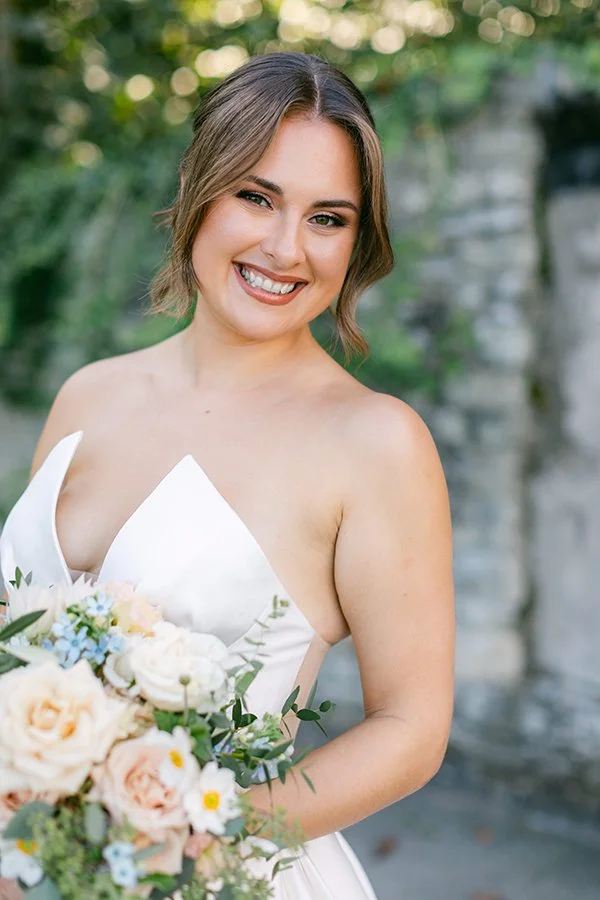 Eine Frau steht lachend in ihrem Brautkleid mit ihrem Brautstrauss.