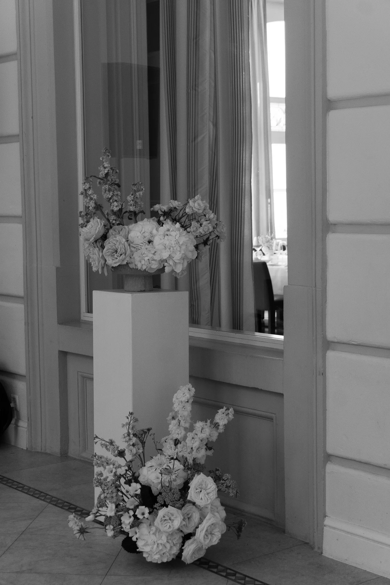 Zwei Blumenarrangements stehen arrangiert auf einer Säule in schwarz weiss.