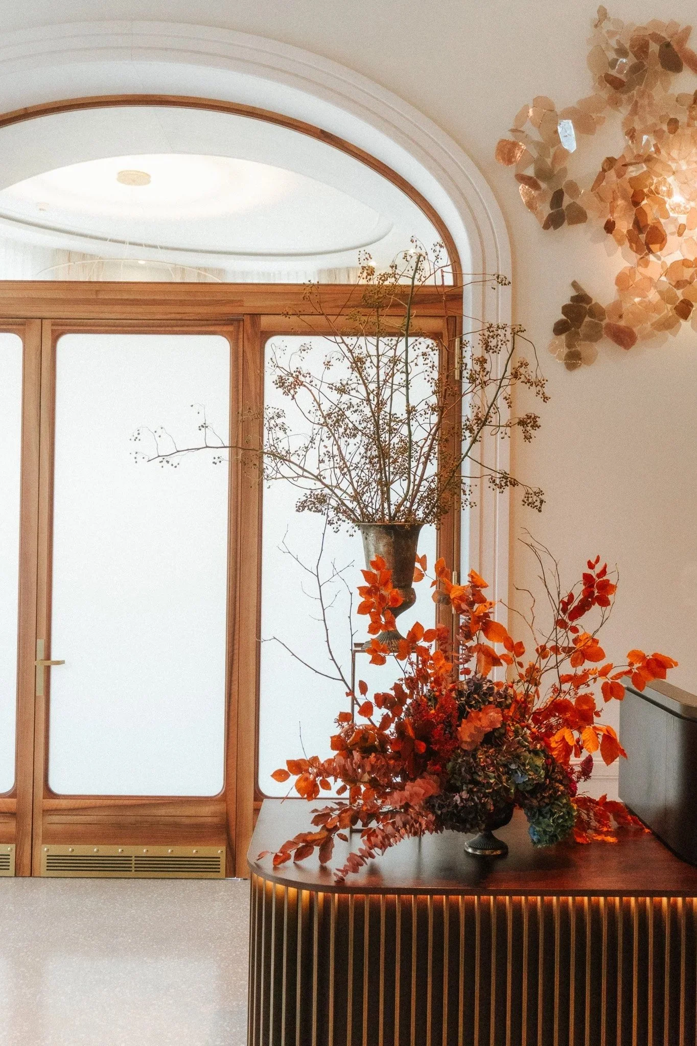 Zwei Blumenarrangements in Orange und Grün stehen auf einem Holztisch in einem hellen Raum.