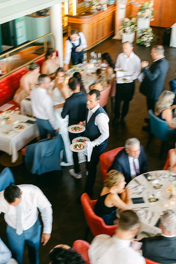 Ein Raum mit Tischen und Menschen und einem Kellner mit Tellern.