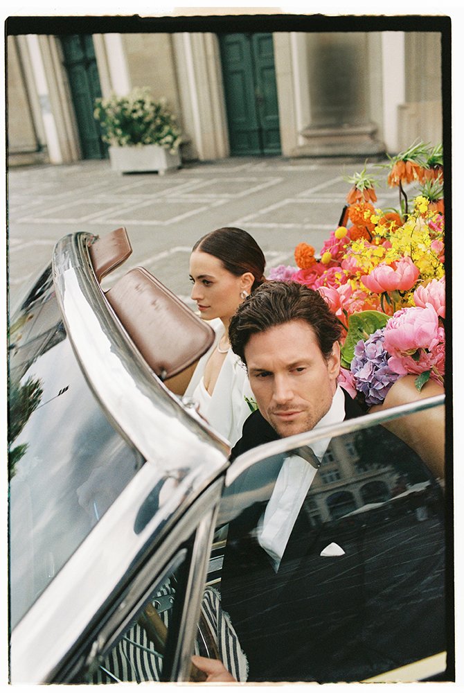 Ein Paar sitzt in einem Oldtimer Cabrio gefüllt mit bunten Blumen.