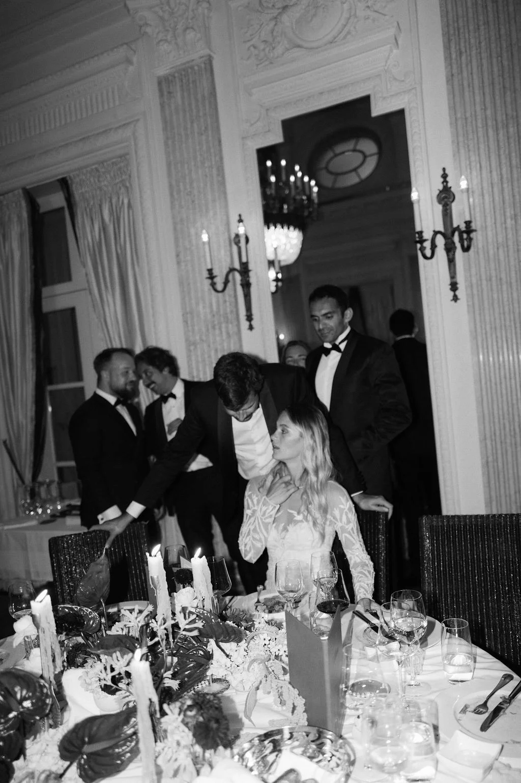 Ein schwarz weiss Bild von einer Frau die an einem eingedeckten Tisch sitzt und mit einem Mann spricht.