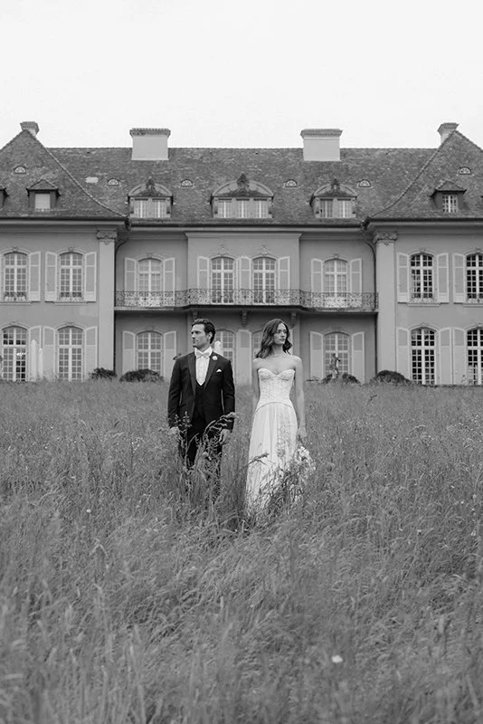 Ein BRautpaar steht auf einer Wiese vor einem alten Gebäude.