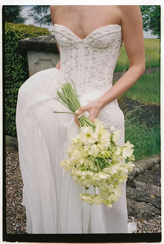 Eine Person in einem Brautkleid hält einen Strauss aus hellgelben Blumen.