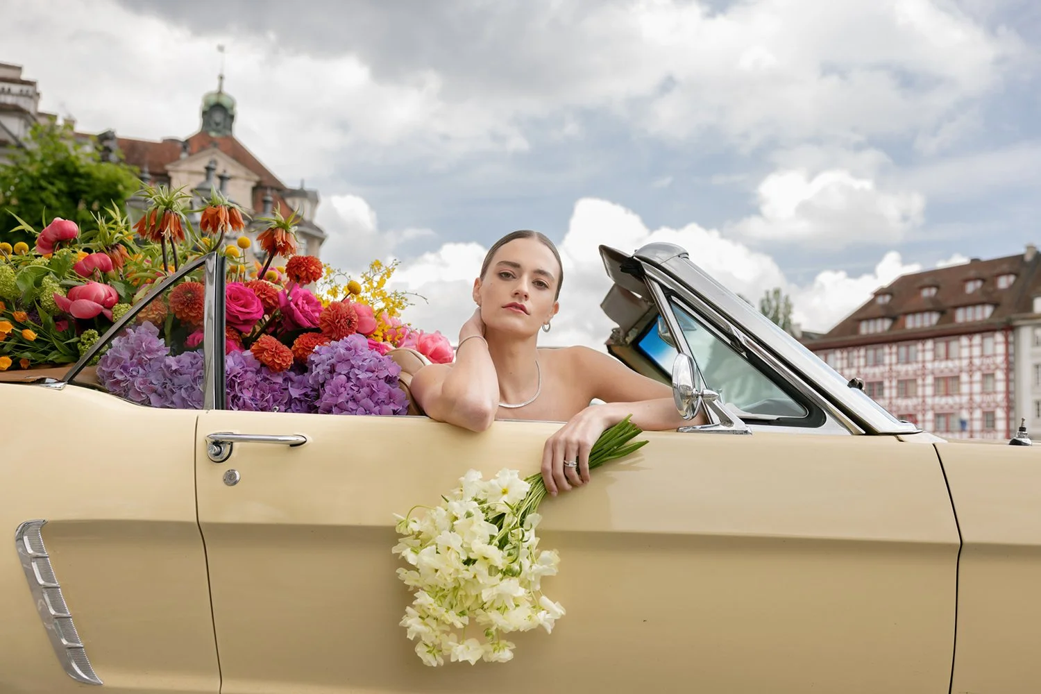Eine Frau sitzt in einem hellgelben Cabrio mit einem Blumenstrauss.