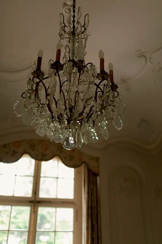 Ein Kronleuchter hängt an der Decke eines hellen lichtdurchfluteten Raums.