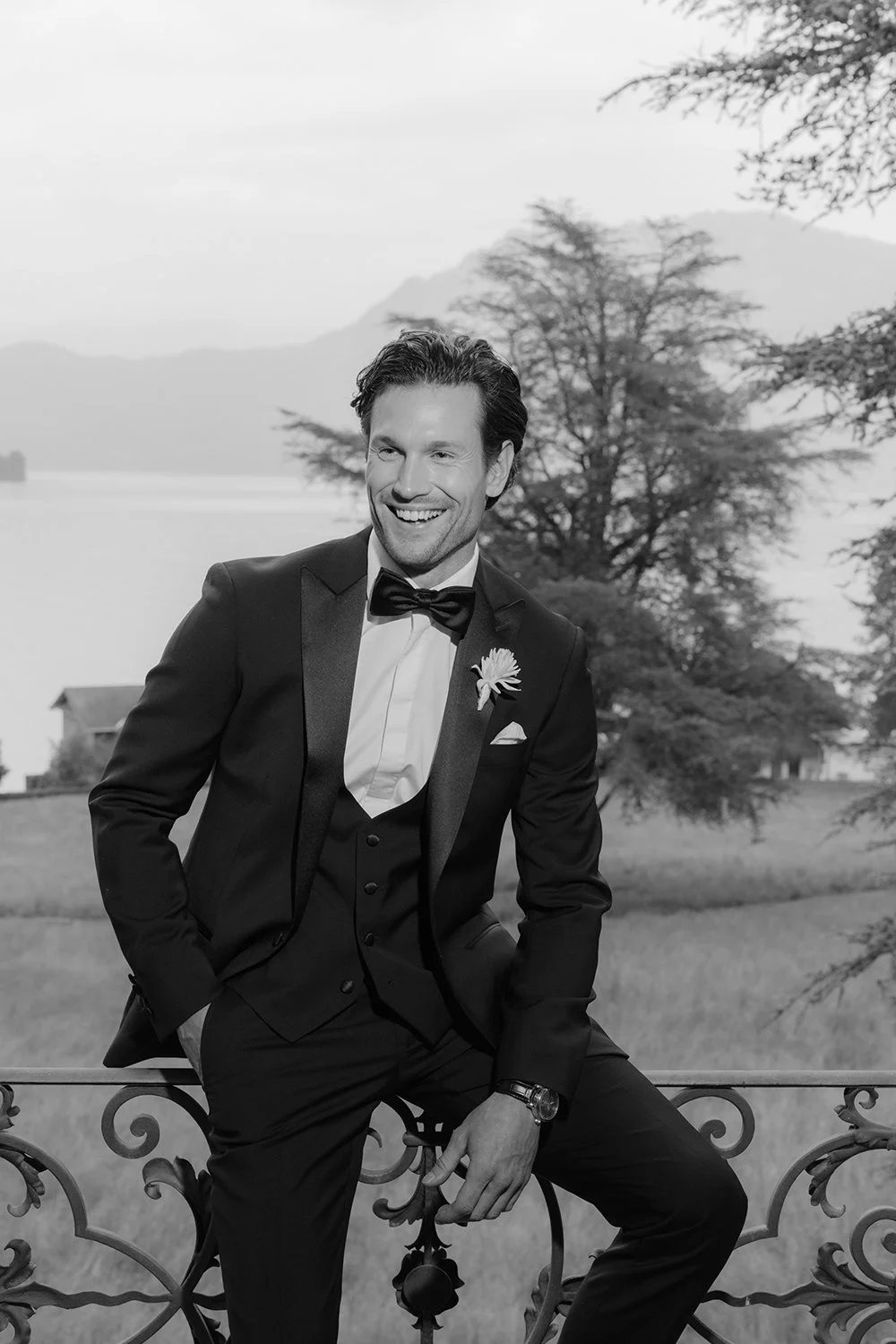 Ein Mann im Anzug sitzt lachen auf einem Geländer.