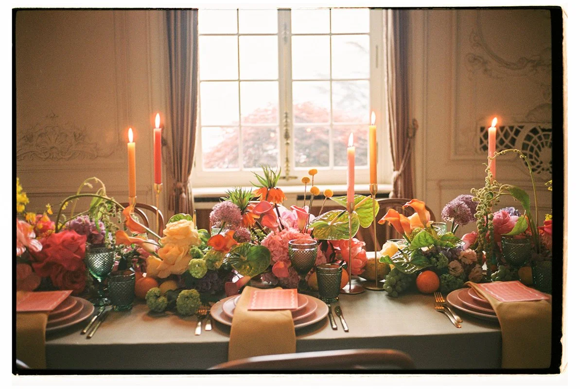 Ein eingedeckter Tisch ist mit vielen bunten Blumen und Kerzen geschmückt.