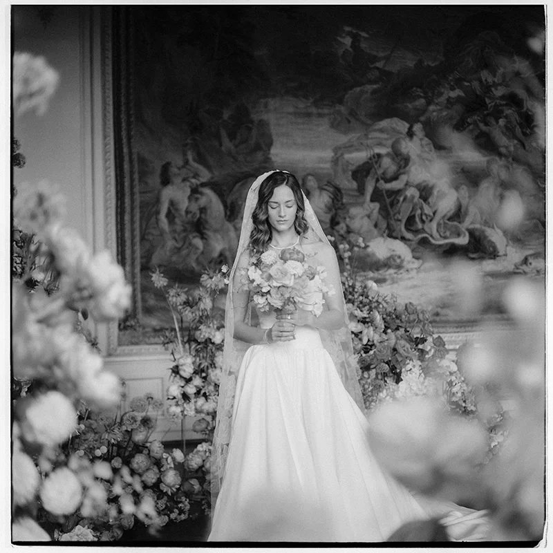 Eine Frau im Brautkleid steht mit dem Brautstrauss inmitten von Blumen.