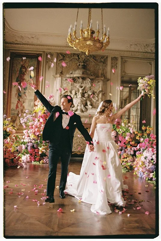 Ein glückliches Brautpaar läuft Hand in Hand durch fliegende Rosenblätter.