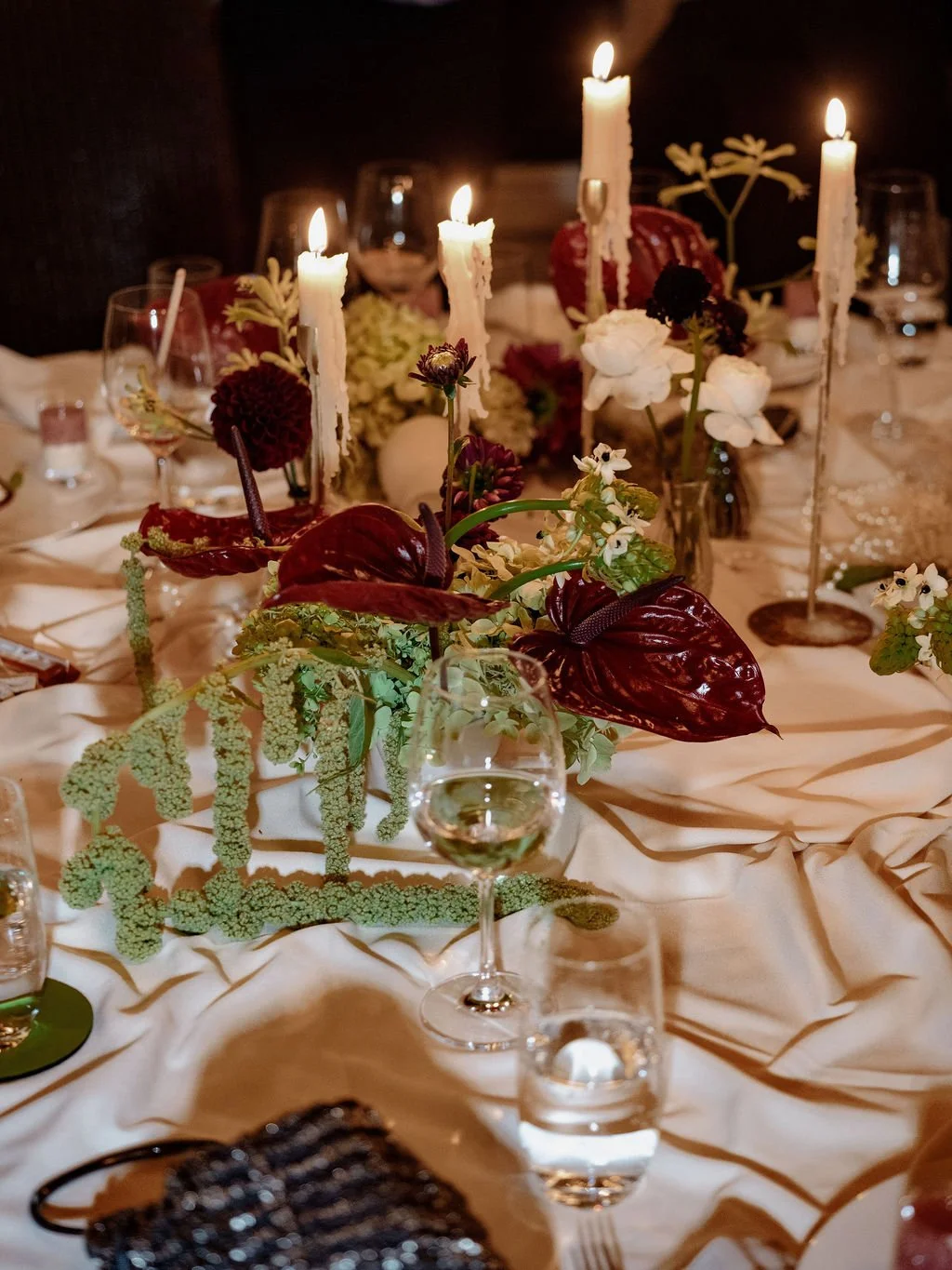 Eine Tischdekoration mit roten und grünen Blumen und Stabkerzen.