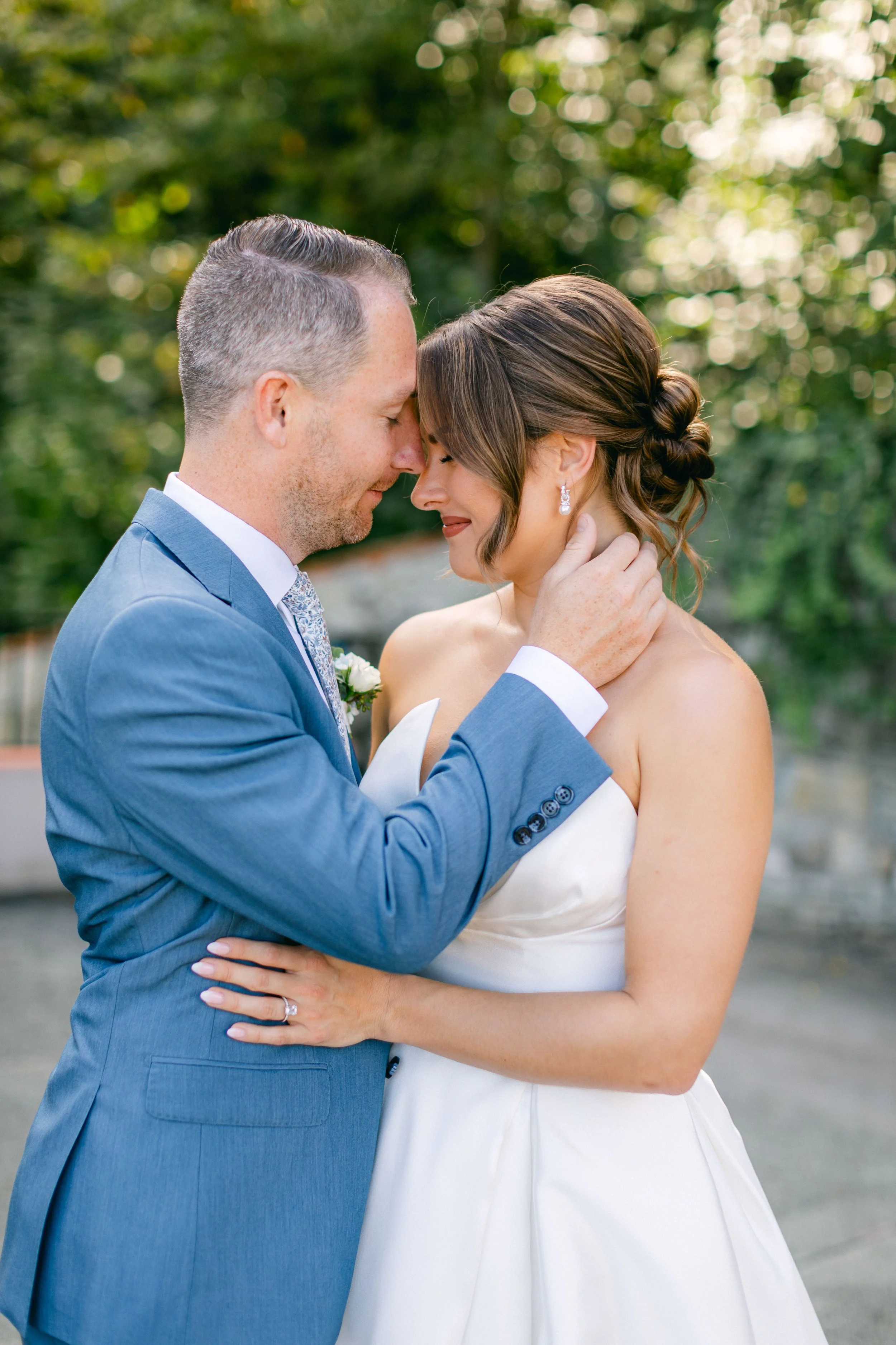 Ein Mann in einem Blauen Anzug küsst die Stirn seiner Frau.