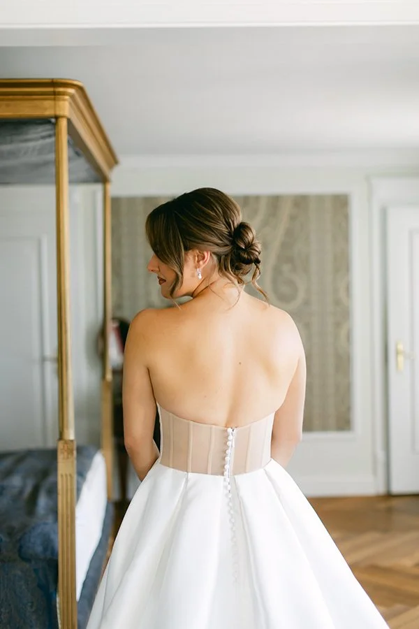 Eine Frau steht in einem Raum in ihrem Brautkleid von hinten.